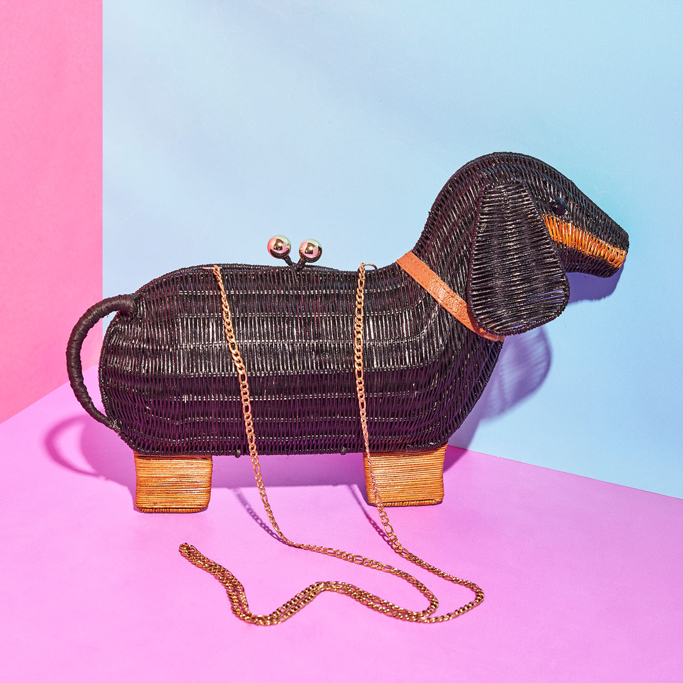 Bangers the sausage dog Wicker Darling clutch with strap on a pink, blue background