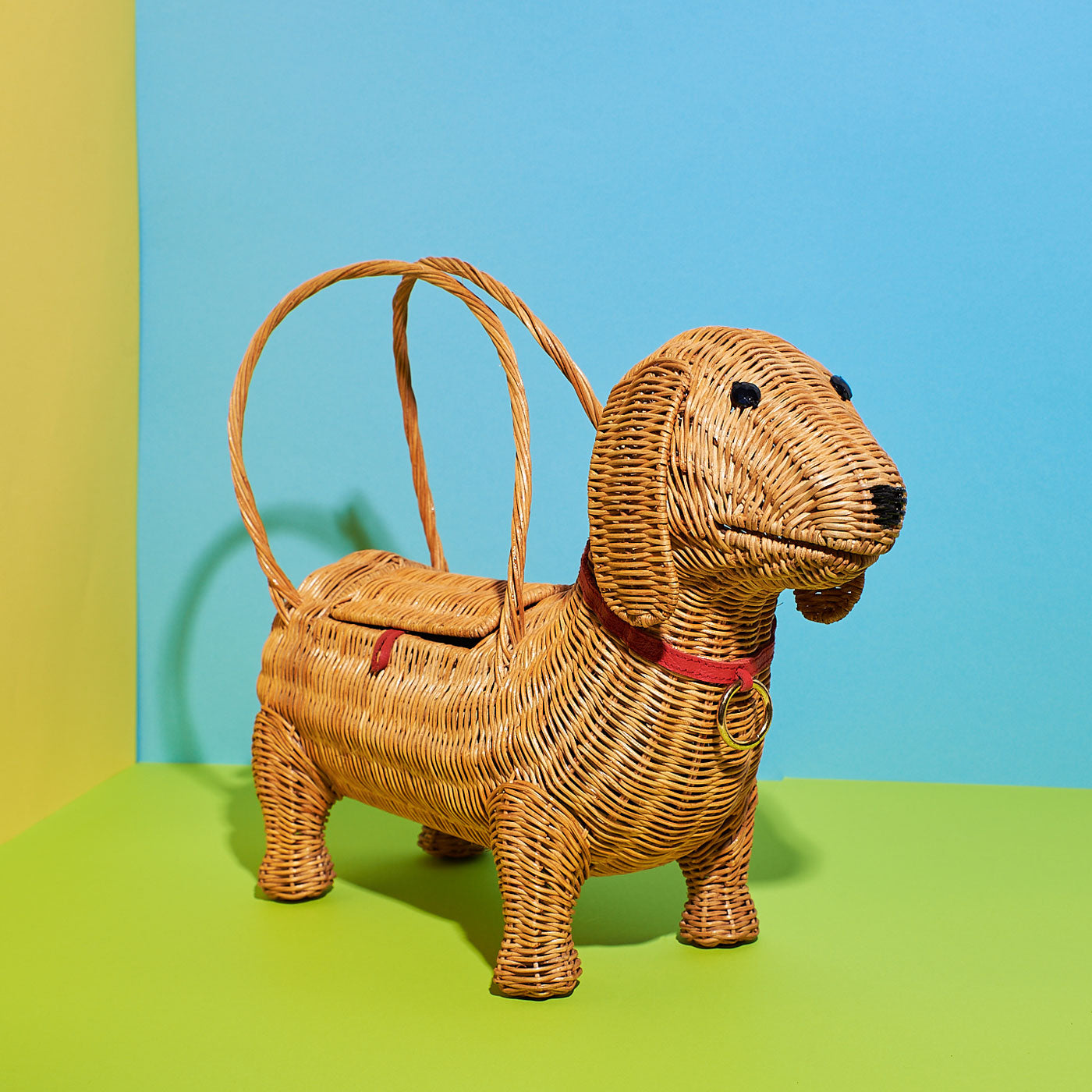 Chorizo the sausage dog Wicker Darling handbag standing on a green background