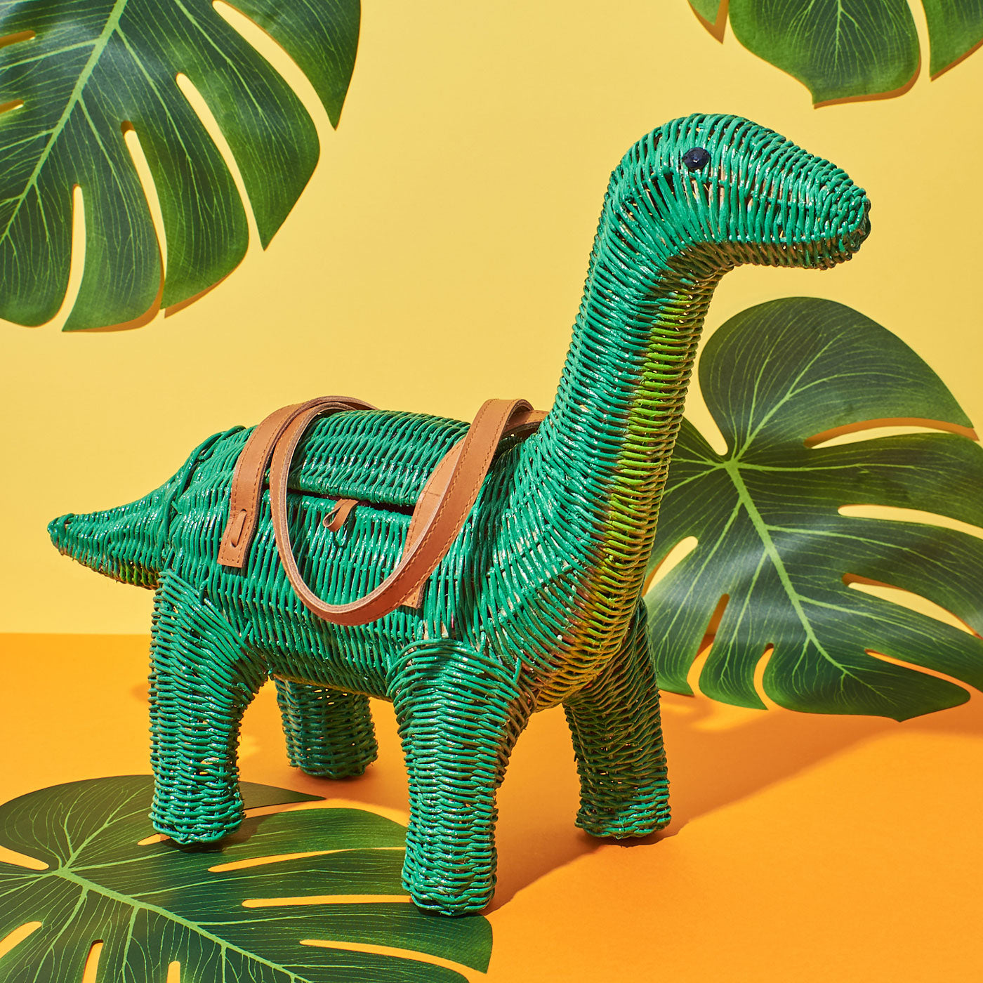 Wicker Darling's green Charlotte Bronte-saurus on a colourful background with green Monstera leaves