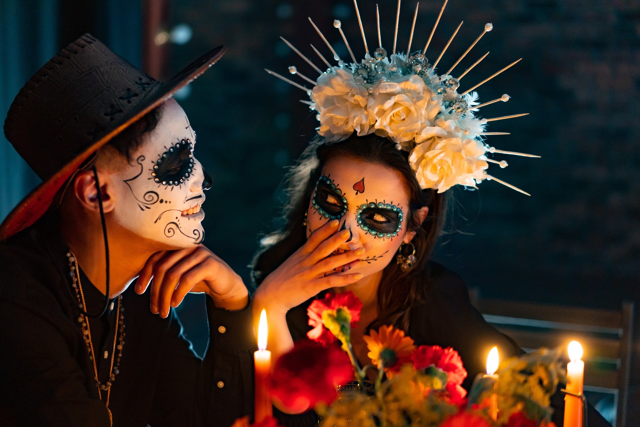 A sweet couple in Halloween costume smiling at each other over a candle lit dinner