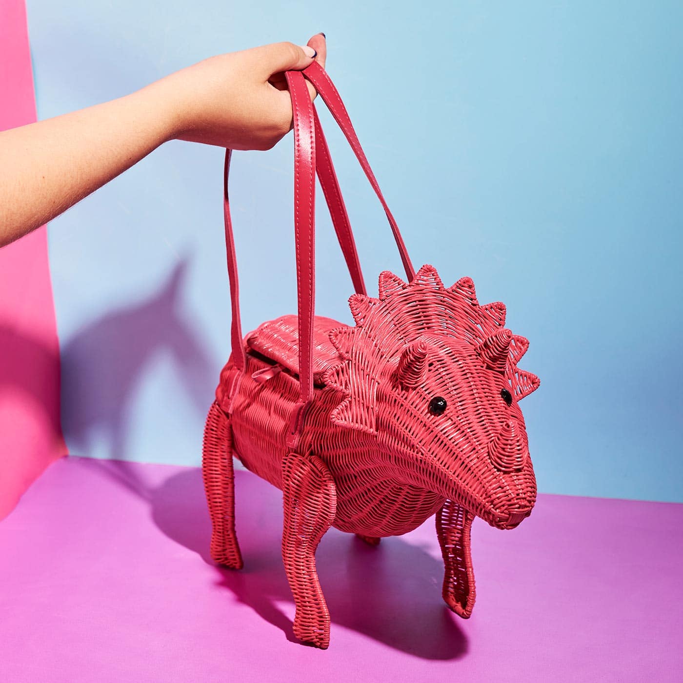 Wicker Darling's Joan the pink triceratops purse on a colourful background