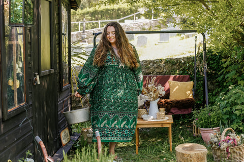 Photograph of a model in a bohemian setting wearing a 1970s style midi dress with exaggerated bishop sleeves in forest green colour.