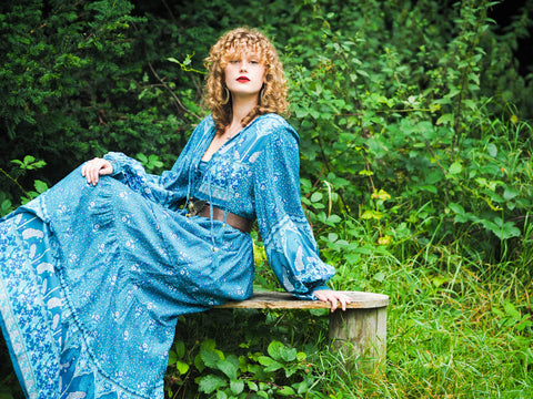 photograph of model wearing blue 1970s style bohemian dress with big balloon sleeves and long tiered flowy maxi skirt