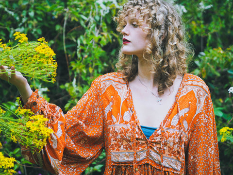 Photograph of a model wearing a 1970s style orange v neck top with balloon sleeves and ornate peacock print.