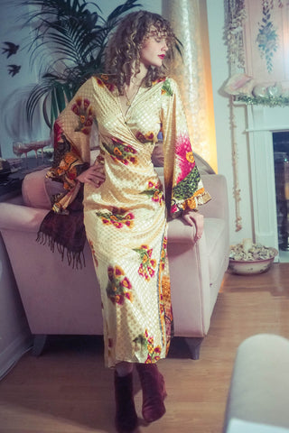 model wears 1970s style venus maxi length wrap dress in gold with peacock feather printed design recycled vintage sari fabric by all about audrey