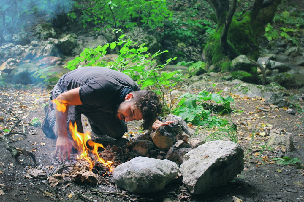 man checking campfire by rocks