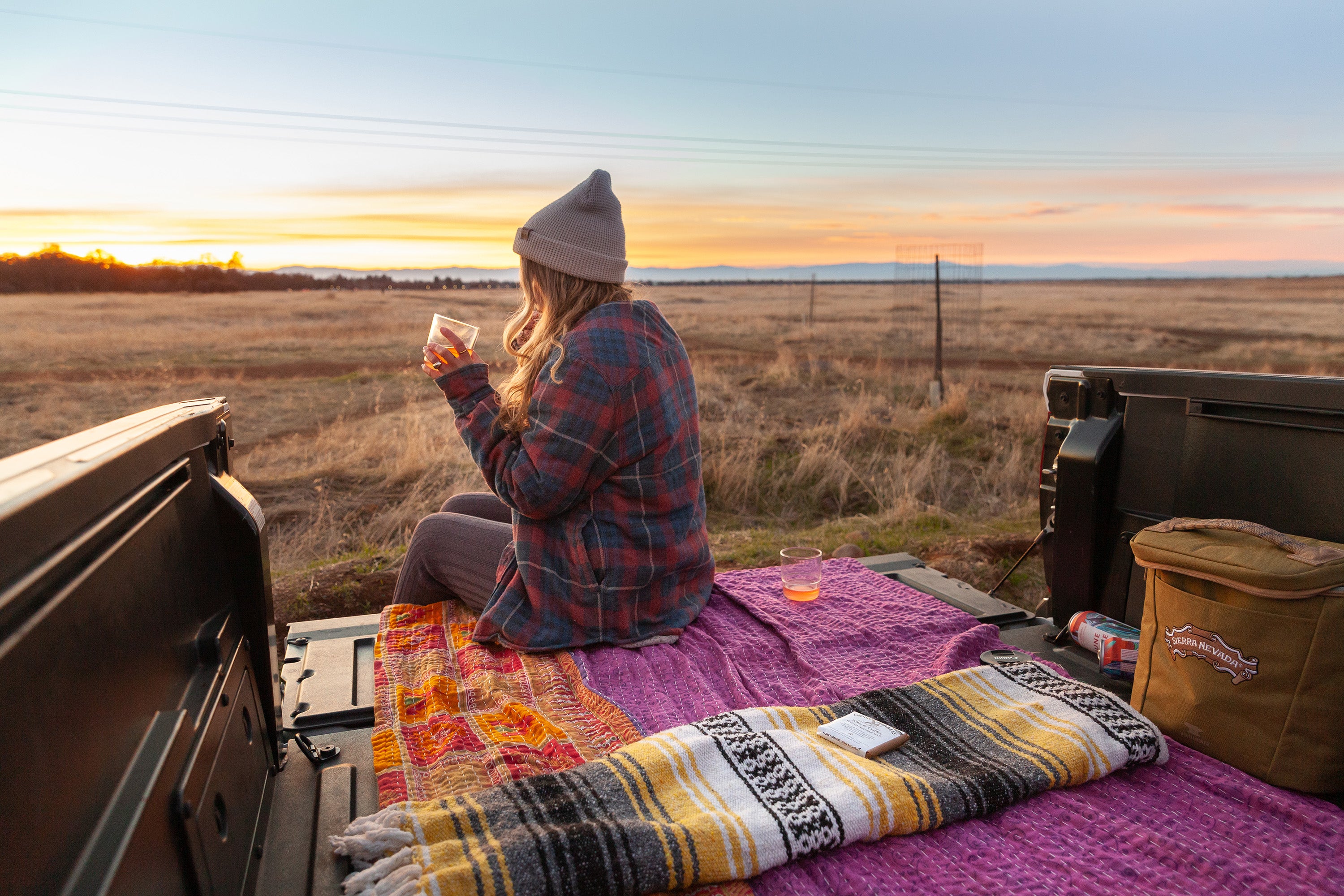 Woman sitting on truck bed with blanket and drink watching the sunset at Bidwell Park in Chico, california