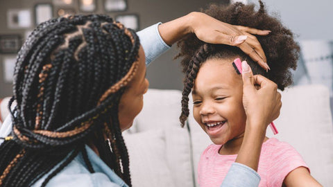 Loving Black mother braiding beautiful Black daughter's hair