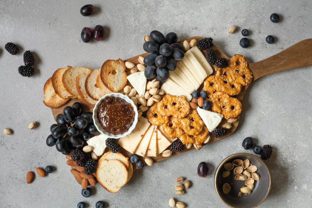 Tabla de madera con quesos y frutos rojos y secos, galletas y panes. Para picotear o presentar una tabla de quesos. 