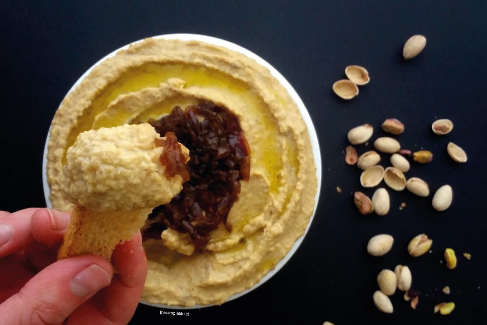 Hummus con base de garbanzo, y topping de cebolla caramelizada, acompañada de pistachos