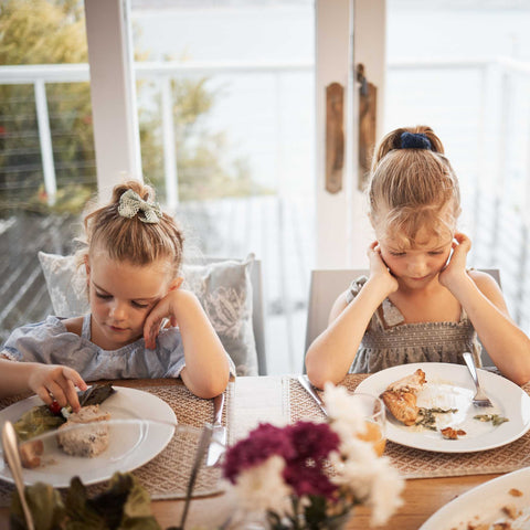 two unhappy kids eating at the dinner table