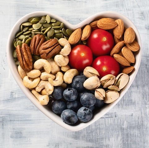 heart-shaped bowl filled with healthy snacks (nuts, berries)