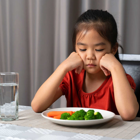 kid looking sad at a plate of broccoli and carrots