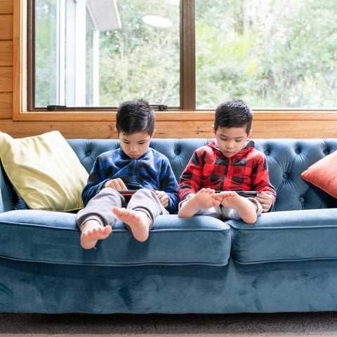two kids on a couch, playing on tablets
