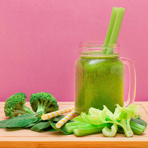 green vegetable smoothie in glass jar surrounded by whole vegetables