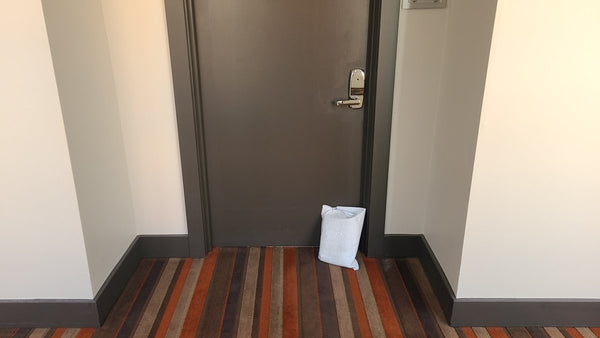 Photo of a brown door, seemingly in an apartment complex. There's a small white bag leaning up against the brown door. The bag has no markings on it, and looks a bit off-white from the journey. It looks like a plain white bubble wrap bag with no info on it. | Kinkly Shop