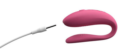 The We-Vibe Sync Lite in profile next to the charging cable. The pin is pointing towards the spot on the Sync Lite where the hidden charging port is. It's on the front of the vibe on the thicker end at the tip. The pin is being pushed in at a slight upward angle. | Kinkly Shop