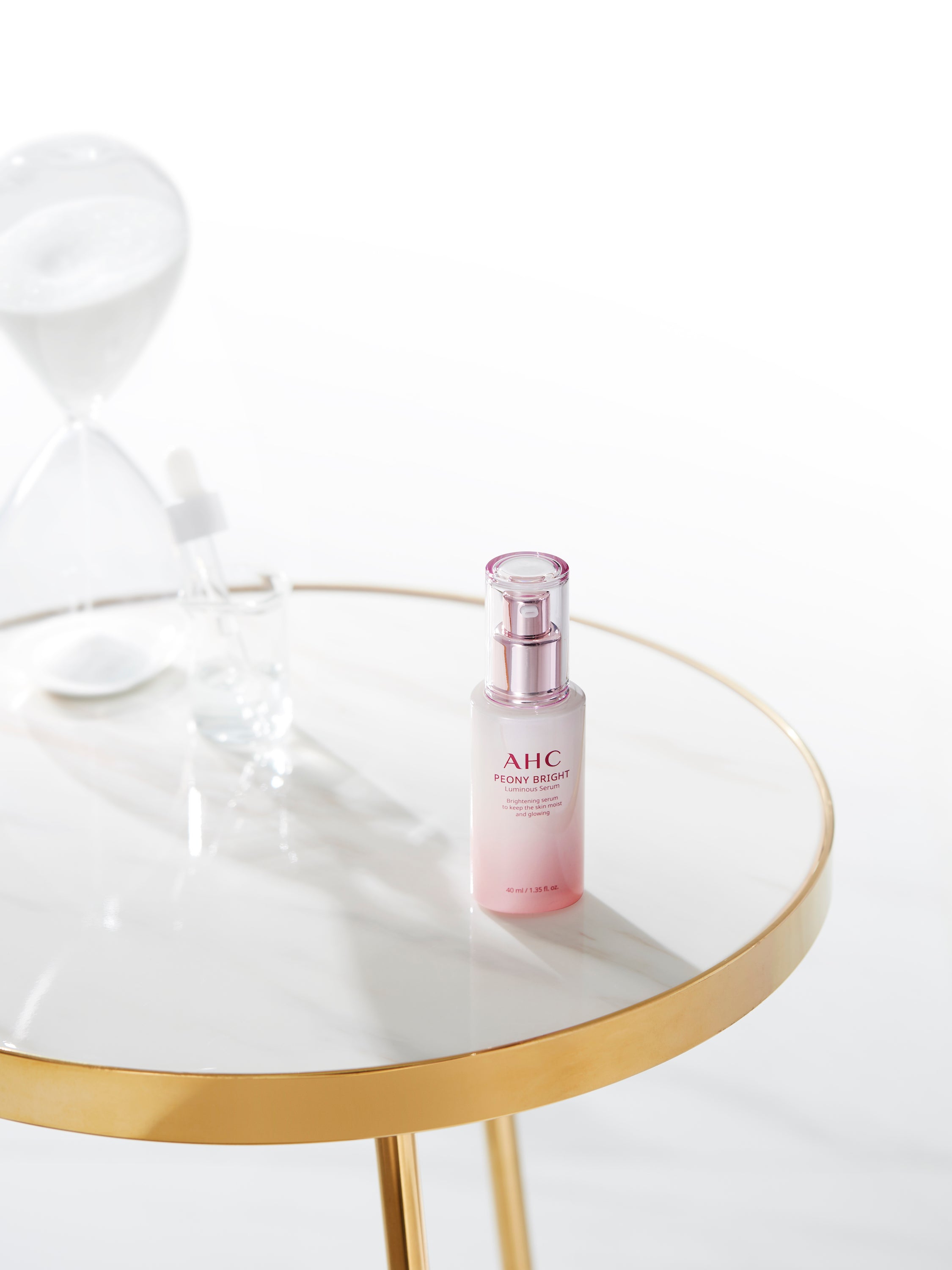 A packshot of AHC Peony Bright Luminous Serum on a white gold table.