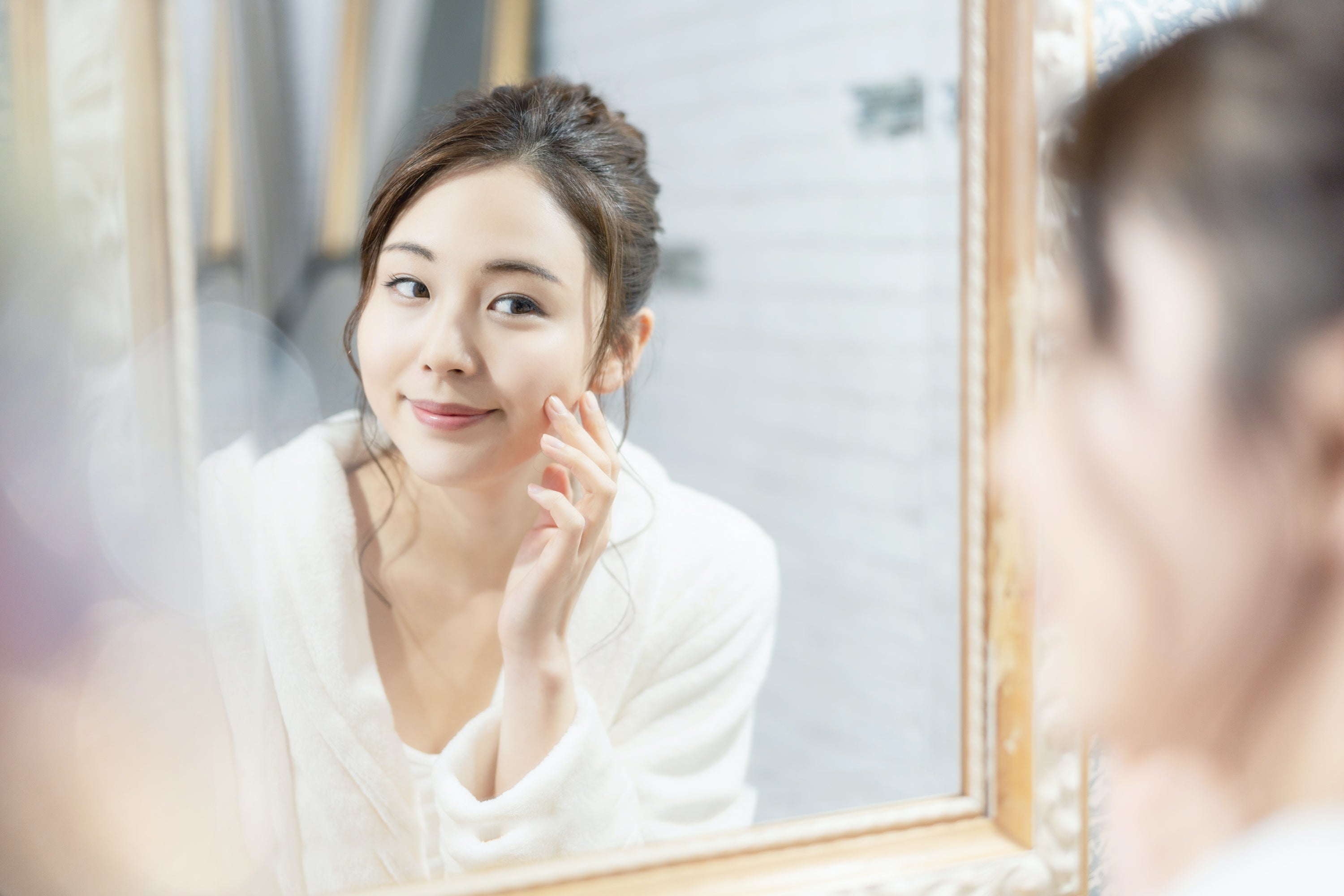 An Asian woman using korean skincare routine for her skin in front of the mirror.