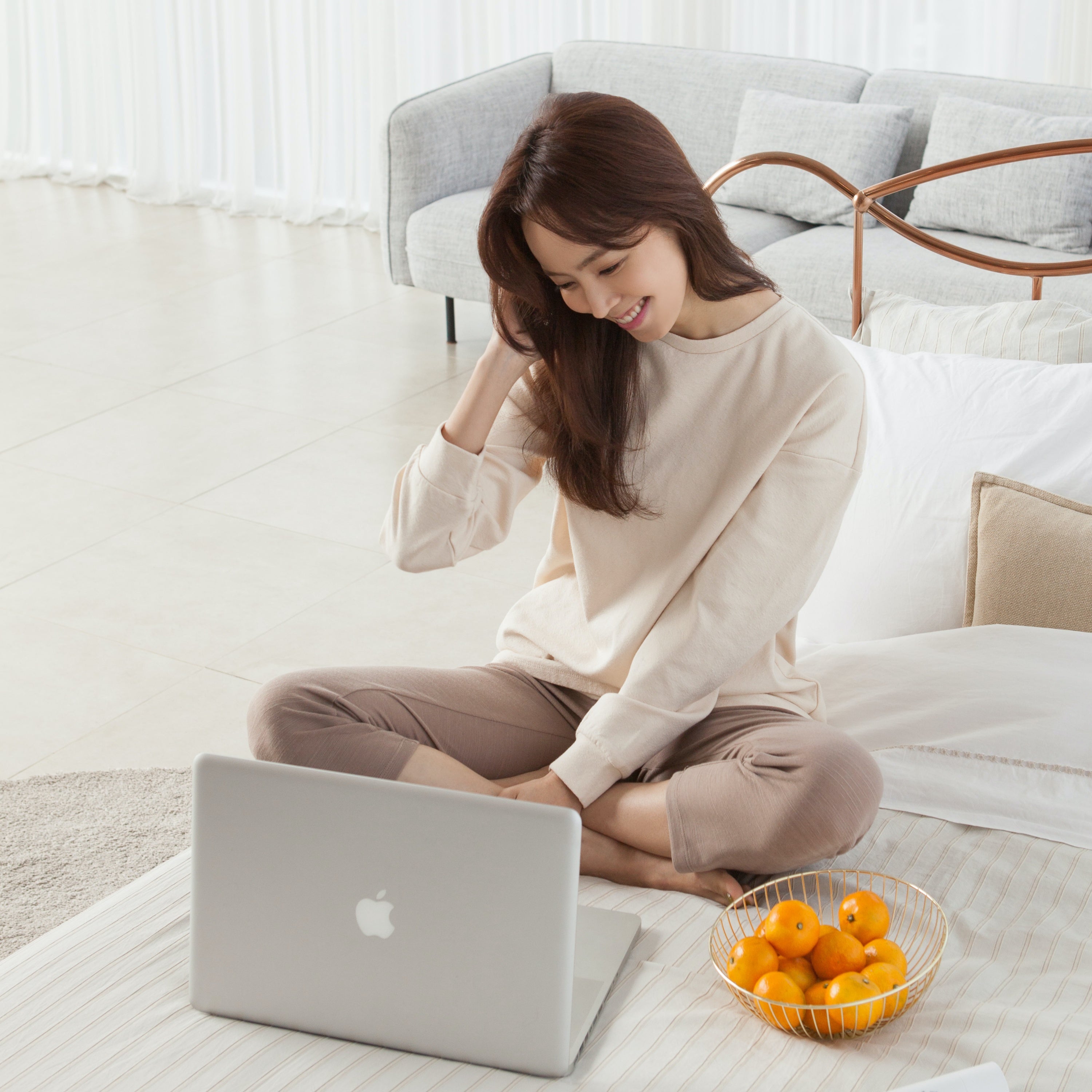 An Asian woman working in front of a laptop with a bowl of oranges