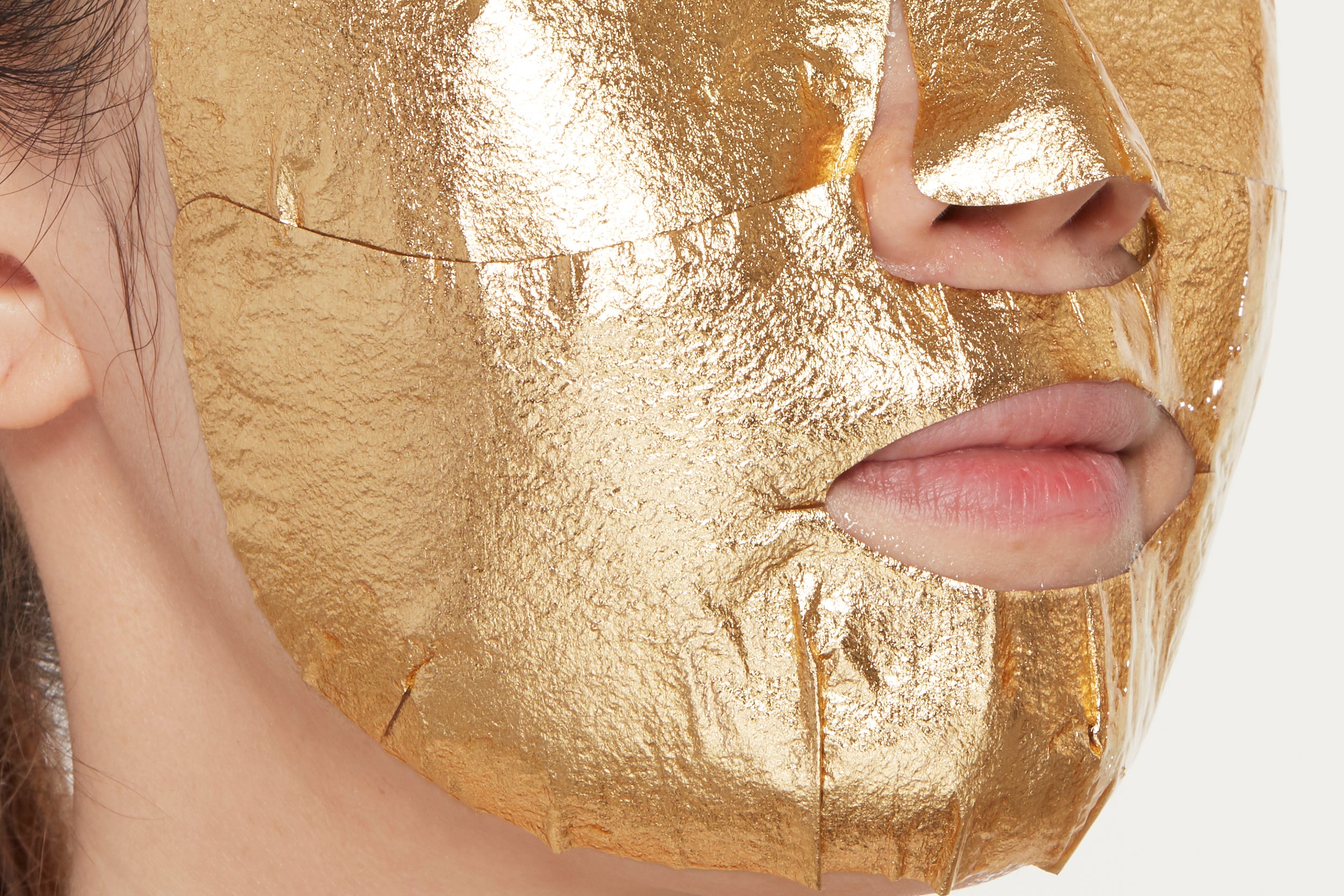 A close-up shot of a woman using a gold mask on her face