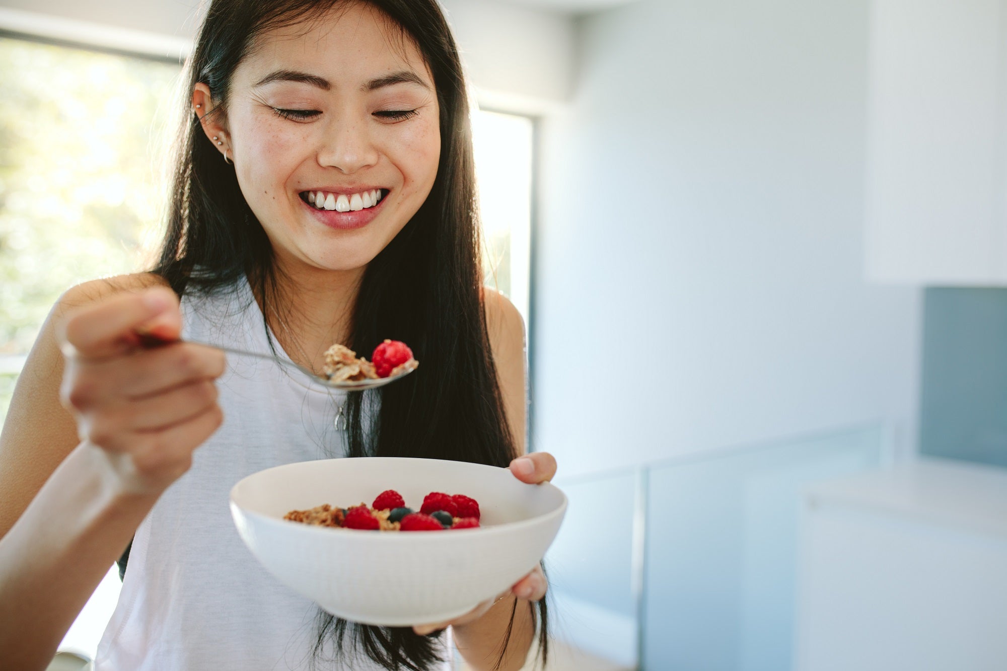 A happy Asian woman eating fruits from a bowl