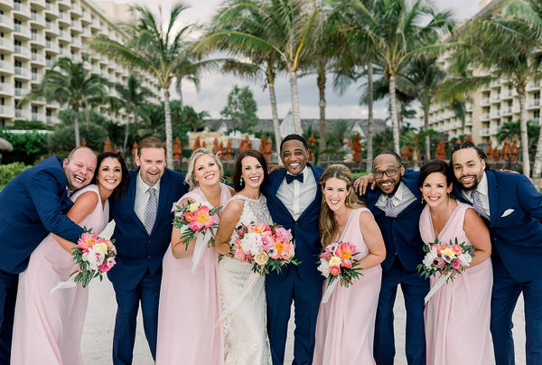 Bridal Party gathered together in front of a tropical background with palm trees. Bridesmaids are wearing dresses from Wedding Shoppe, Inc.