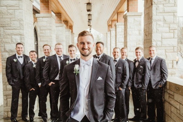 Groom in tuxedo, white vest, and white bowtie. Groomsmen wearing tuxedos and black bowties.