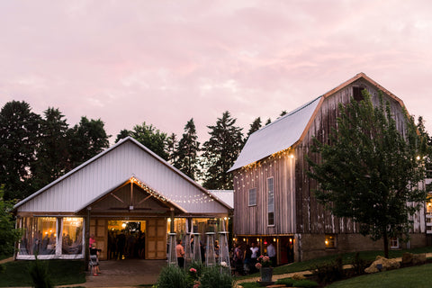 Refurbished barn and building set up for a wedding reception. Twinkly lights drape across the side.