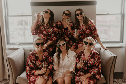 Bride and Bridesmaids wearing matching robes and heart-shaped sunglasses, holding glasses of champagne.