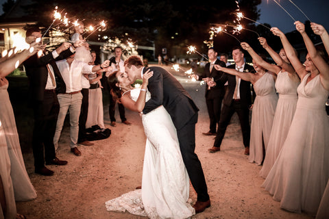 Bride and Groom dipping for a kiss, surrounded by two rows of guests holding sparklers.