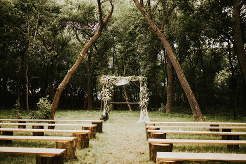 Ceremony is set up in a wooden area with simple wooden pews and a decorated pergola