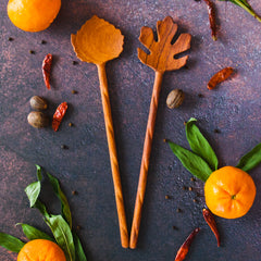 Leaf Shaped Wooden Salad Servers - Set of 2- on a dark background with orange citrus fruit, red chilis and green leaves