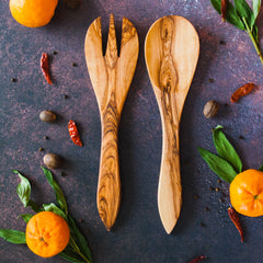 Olive wood salad servers on a dark rusty background with orange citrus, red chili peppers and green leaves