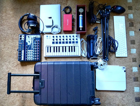 A flat lay photo of a travel luggage and an array of music production equipment