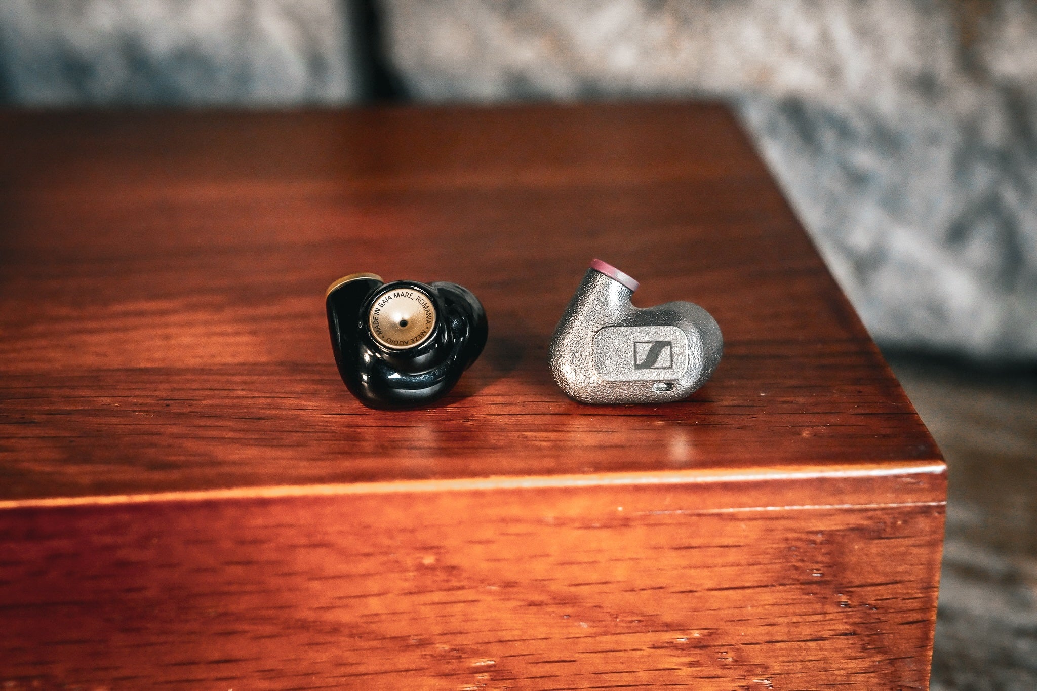 Meze Advar and Sennheiser IE 600 resting on a wooden table with a stone wall in the background from the Bloom Audio gallery