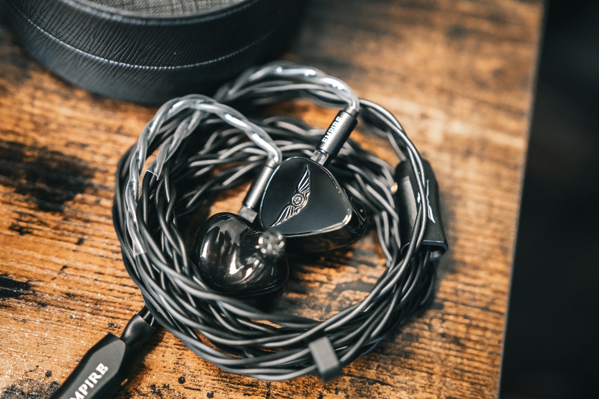 Empire Ears Raven coiled with its cable on a stained wooden table with its case next to it from the Bloom Audio gallery