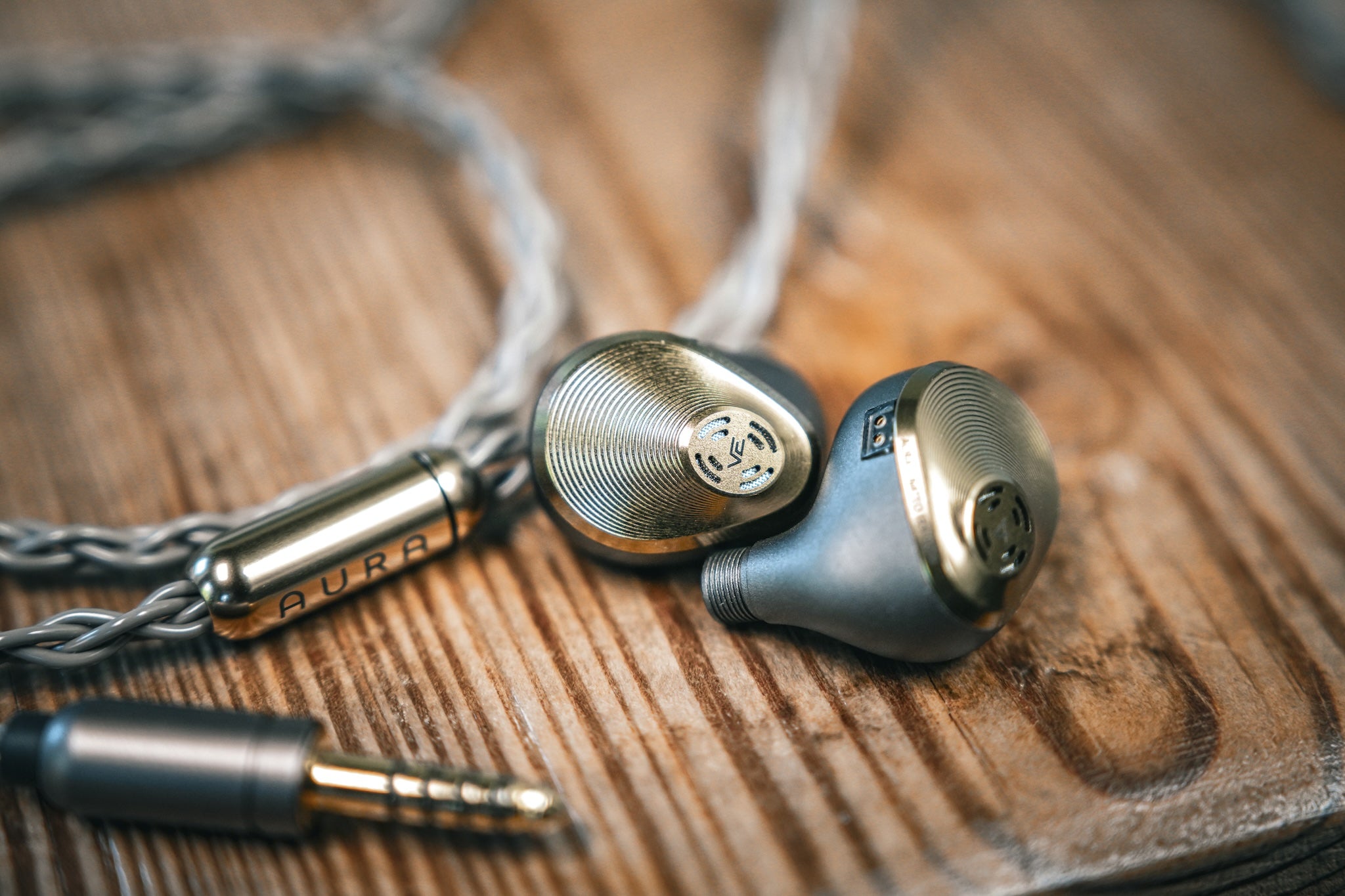 Vision Ears Aura IEM next to its cable on a knotty wooden stool from the Bloom Audio gallery