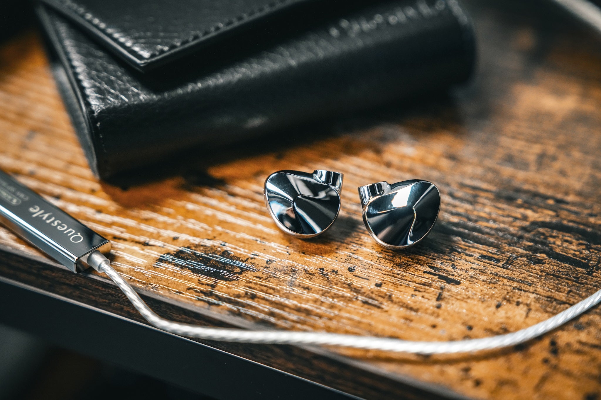 Questyle NHB12 on top of a wood stained table with its cable and case next to each other from the Bloom Audio gallery