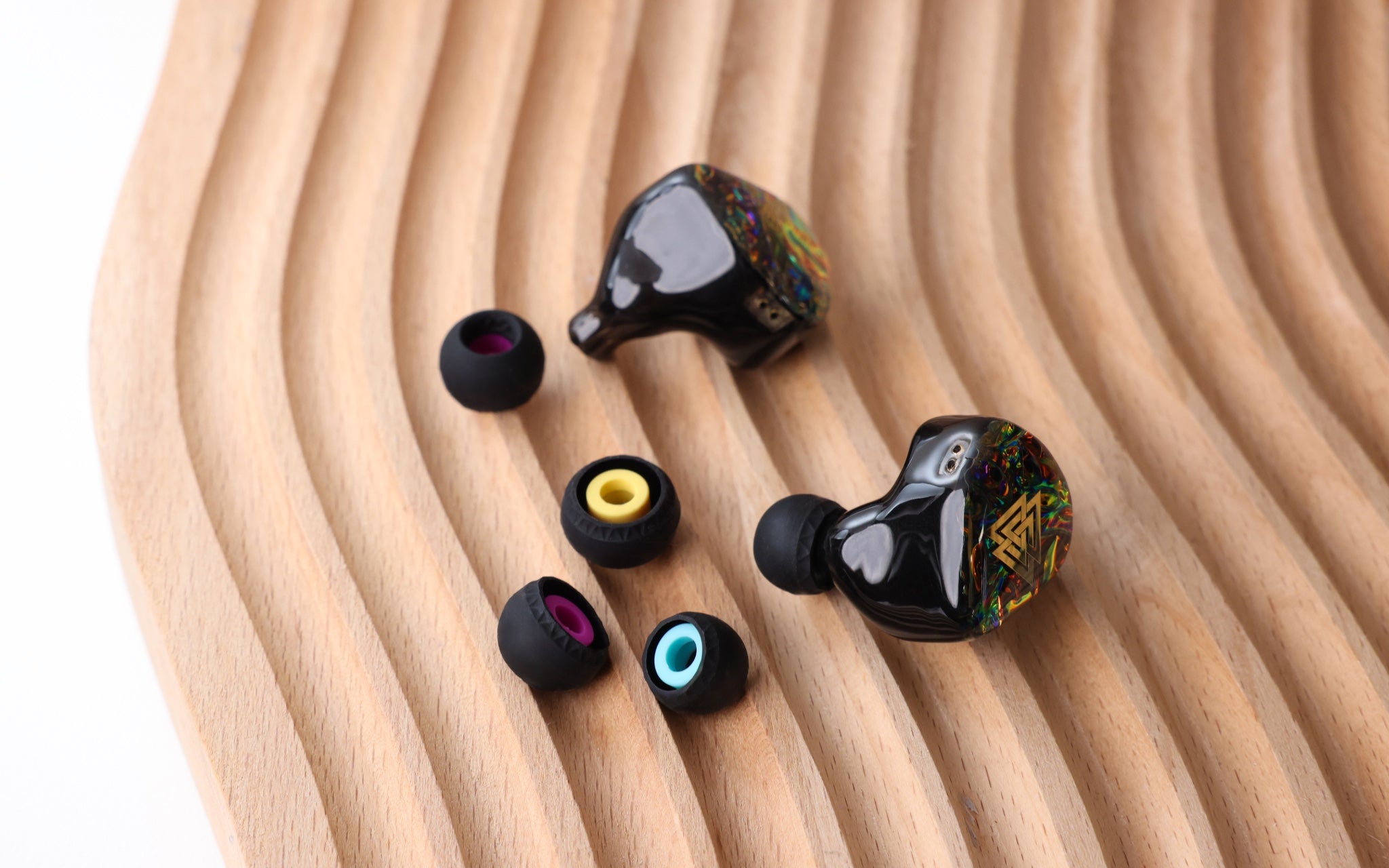 Eletech Baroque assorted sized eartips with Empire Ears Odin earphones on wavy-patterned wood block tray