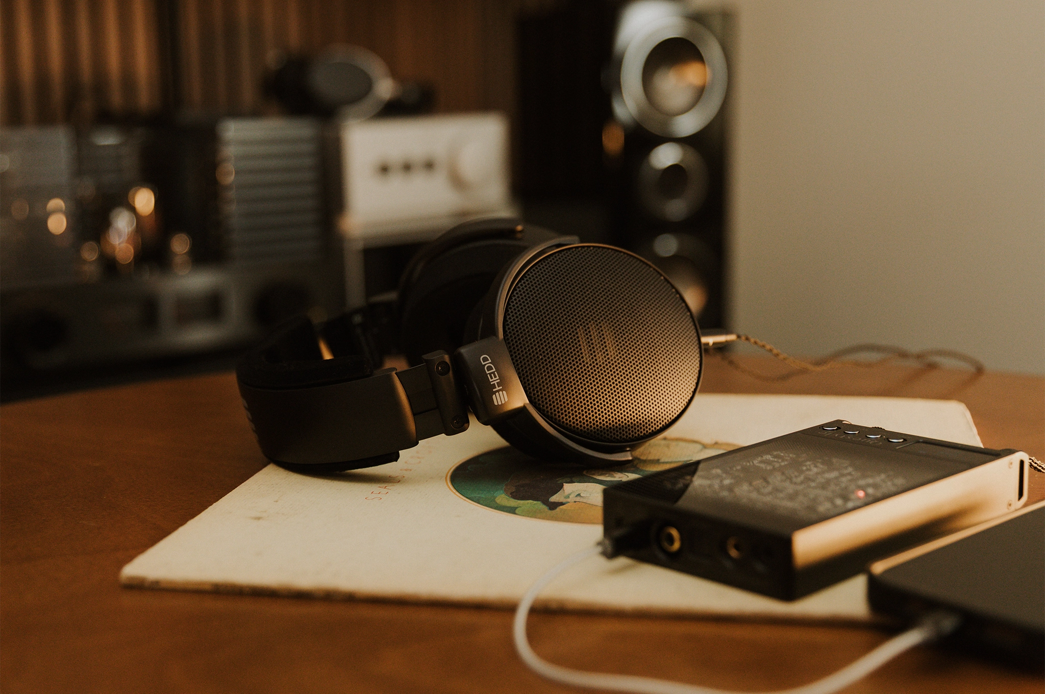 HEDD D1 headphones lying on round wooden table plugged into Questyle Sigma Pro DAC/Amp on top of vinyl record