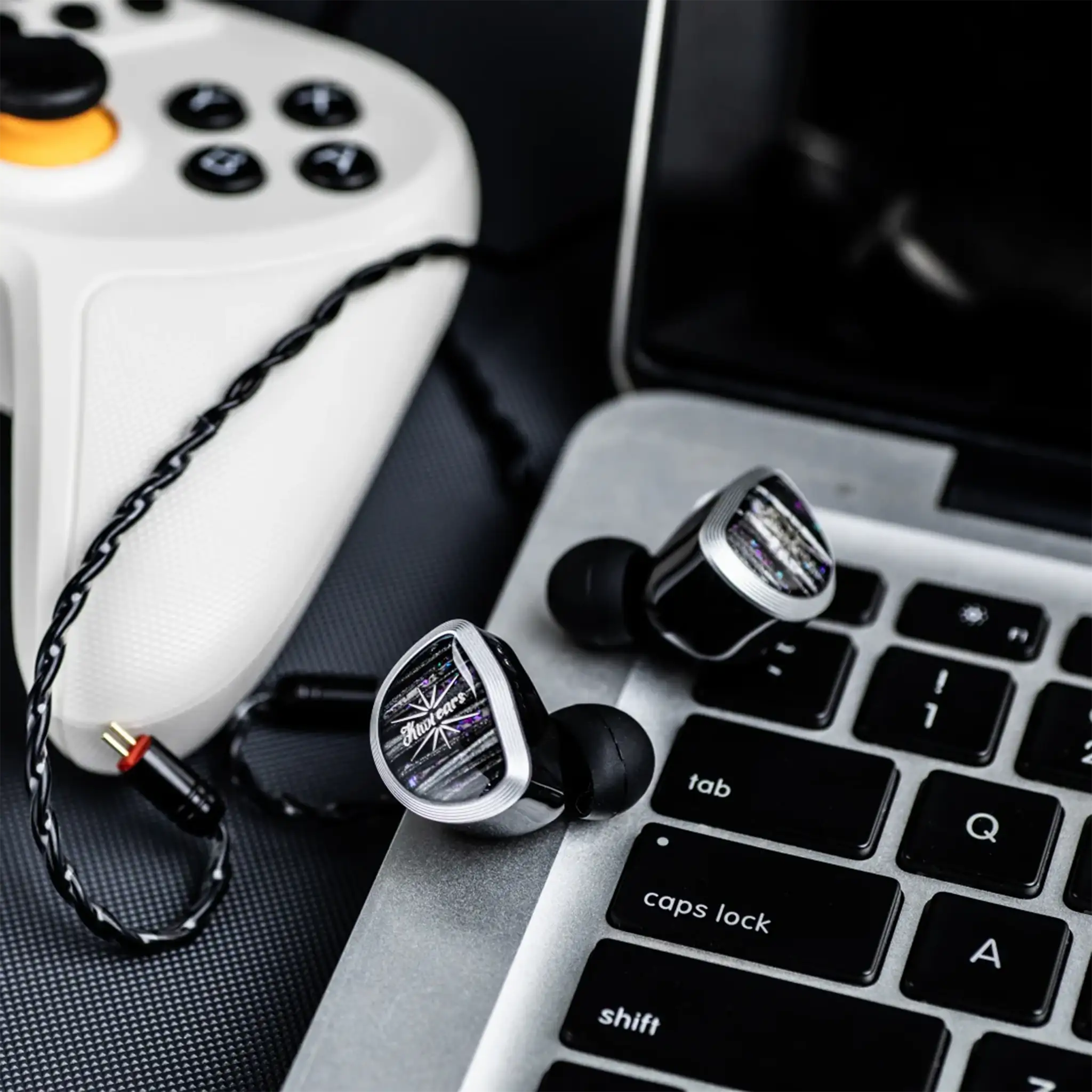 Kiwi Ears Aether IEMs sitting on laptop keys next to cable and gamer controller