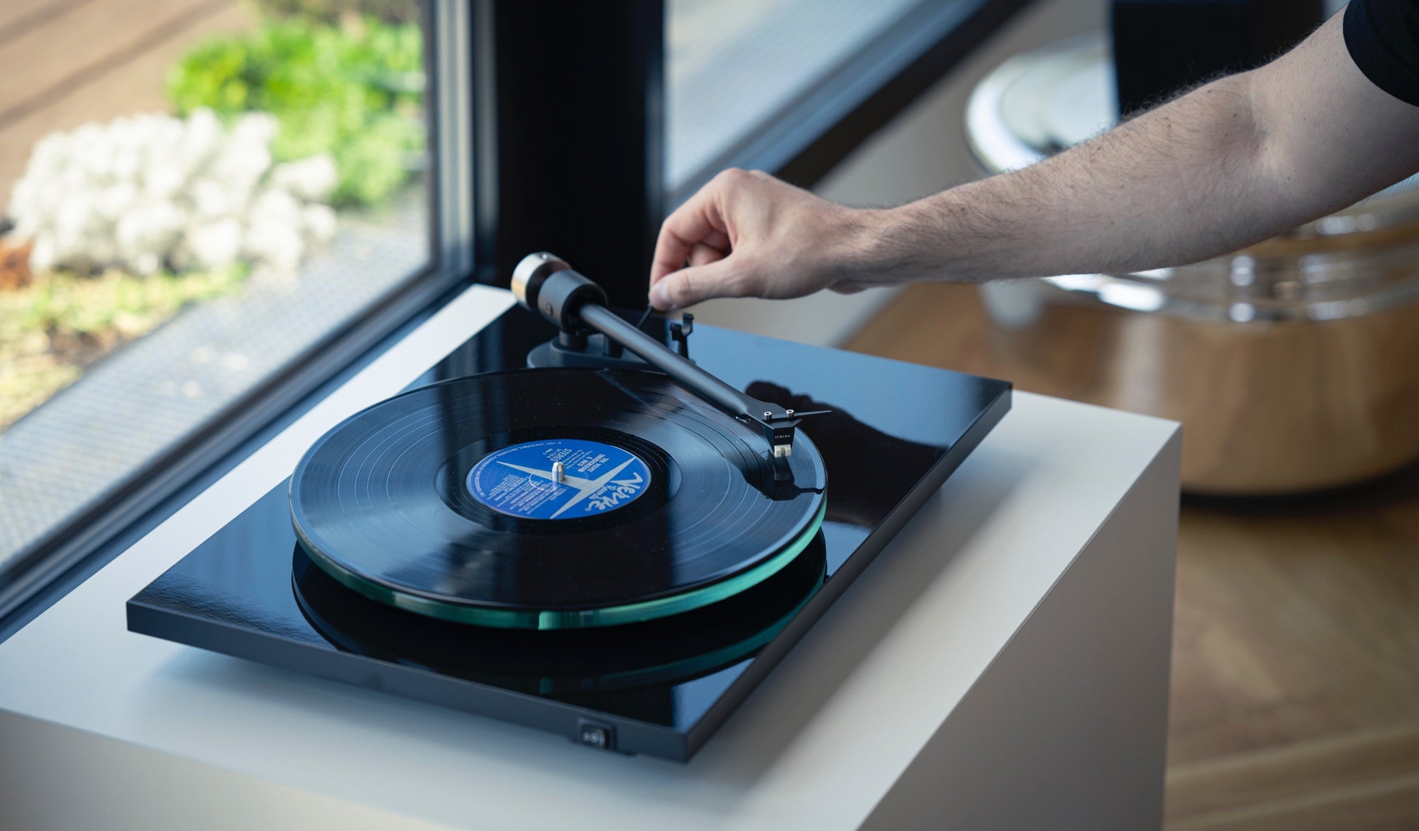 Pro-Ject T2 black on white decorative cabinet in living space with human lowering tonearm