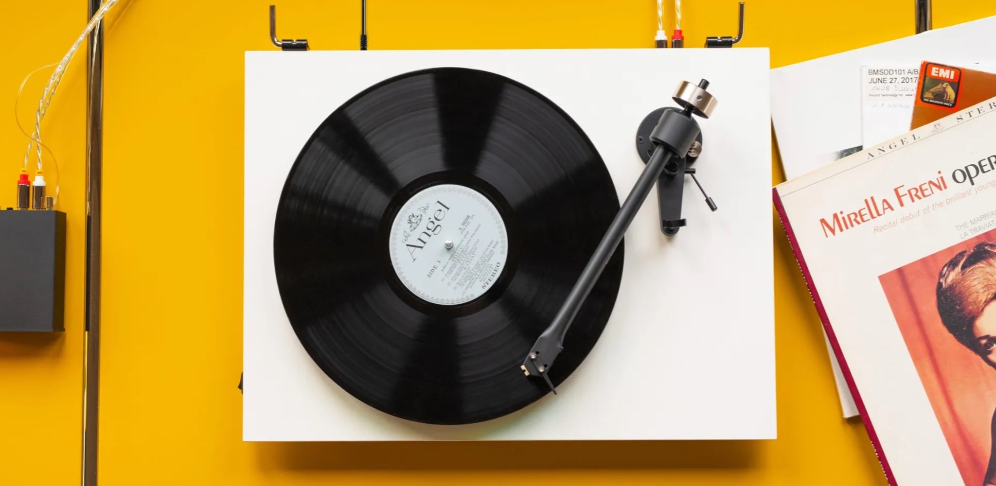 Pro-Ject T2 white bird's eye over yellow cabinet with vinyl jackets and connected external preamp