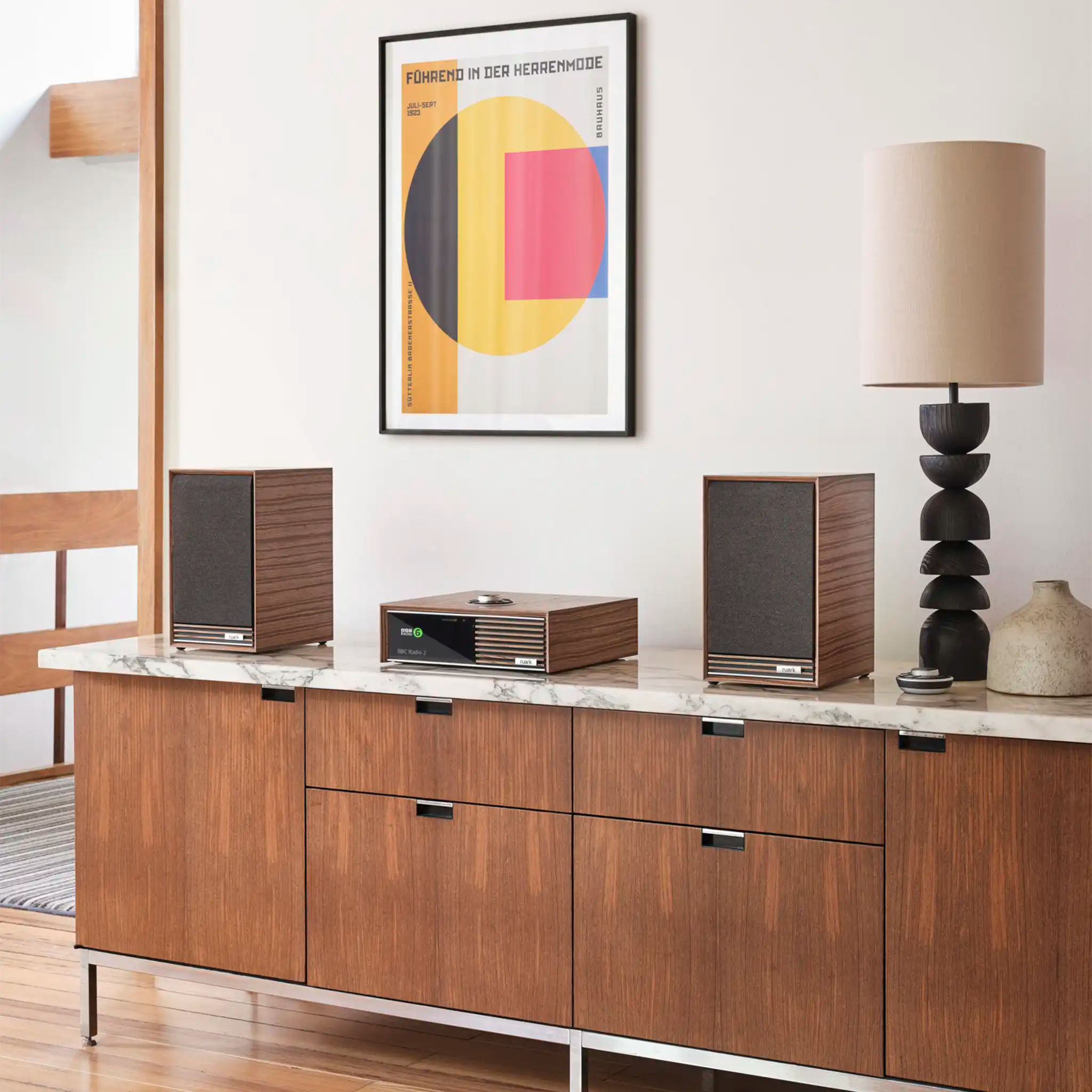 Ruark Audio R610 console in walnut sitting front right 3 quarter angle on wooden table with marble top with lamp and ruark bookshelf speakers