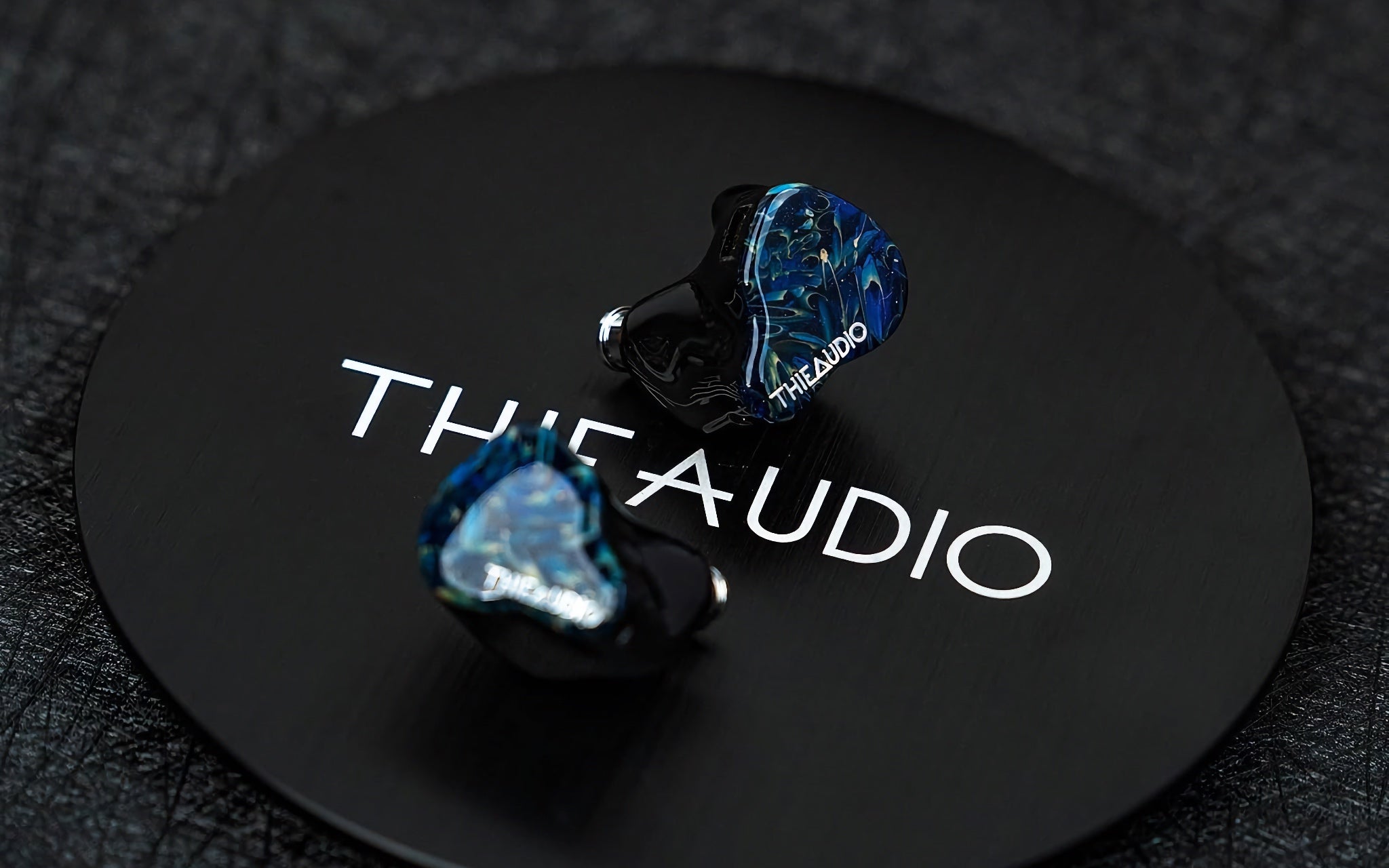 Thieaudio Hype 2 blue IEMs on black cylindrical plate with logo