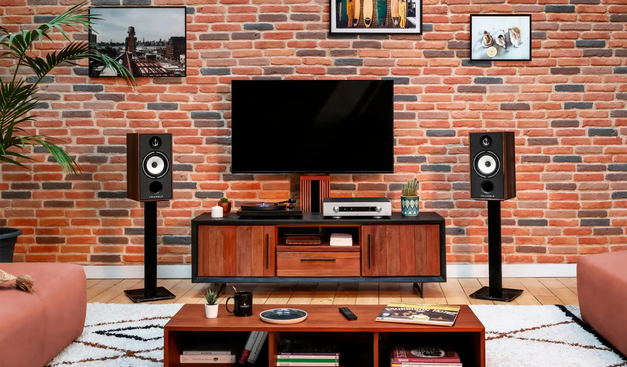 Triangle Audio Borea BR04 speakers in black ash sitting on black stands between black and walnut tv entertainment stand with brick wall behind