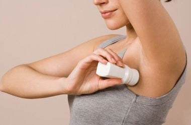 Woman wearing grey vest rolling deodorant under her arms.