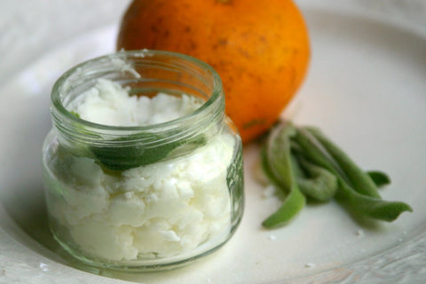 Homemade deodorant in glass jar with herbs and orange in the background.