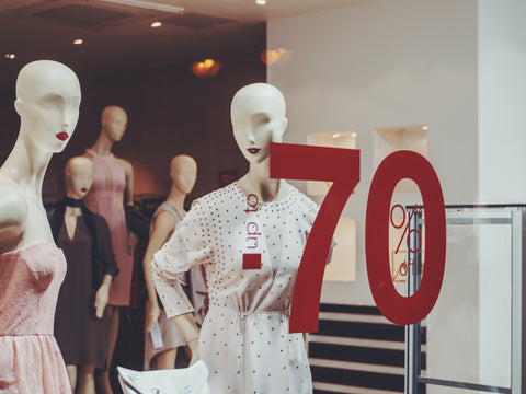 White and pink dressed mannequin in shop window with 'up to 70% off' written on window.